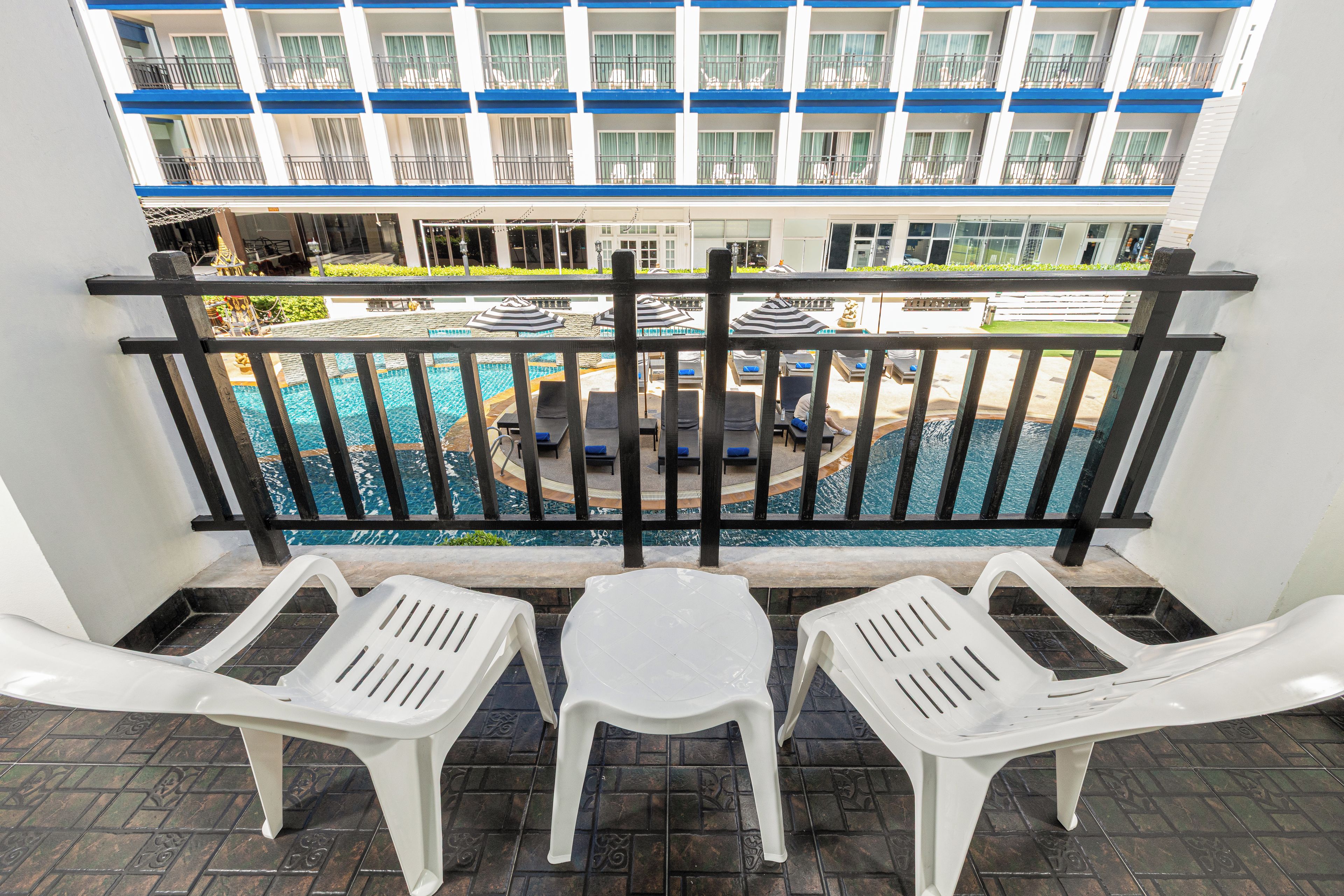 A balcony with a view of a swimming pool, lounge chairs, and a building with balconies in the background.