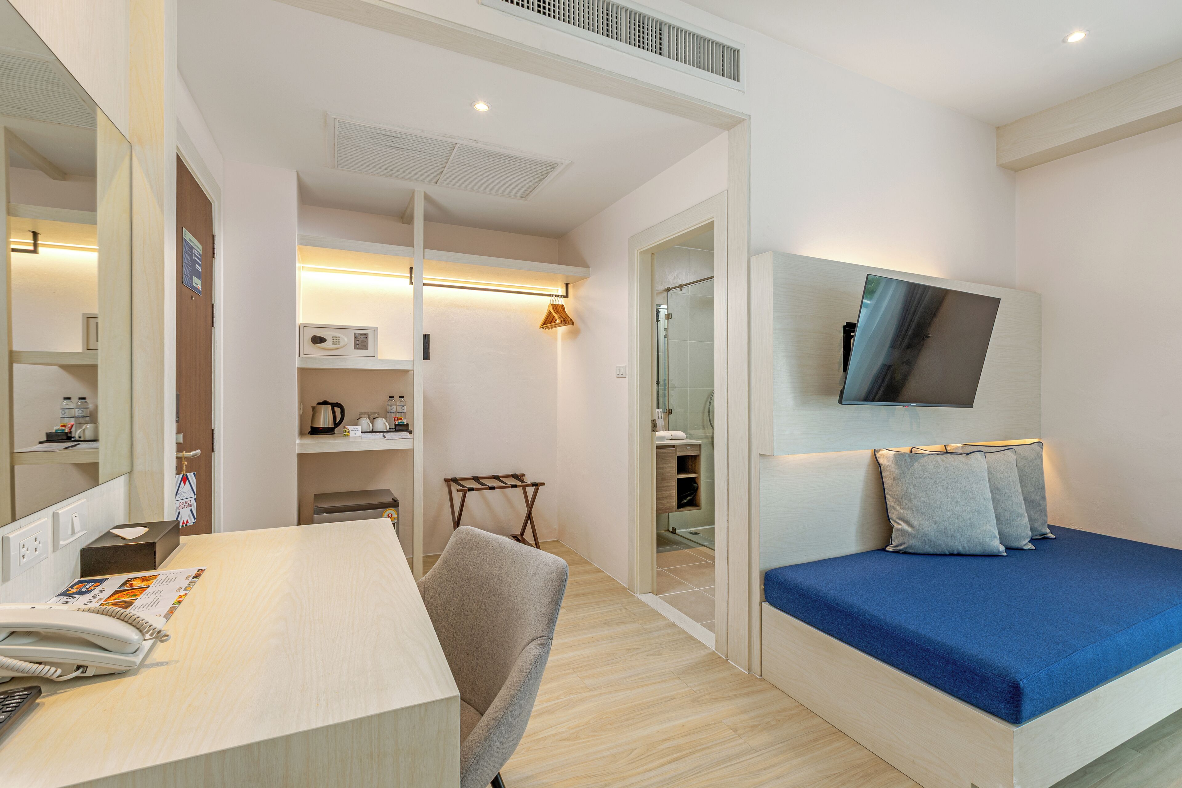 A modern hotel room with a bed, a desk with a telephone, a chair, a TV mounted on the wall, and a small seating area with a table and chairs.