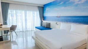 A modern hotel room with a large bed, a desk, and a view of the sea through a window. - Amata Patong (Patong)
