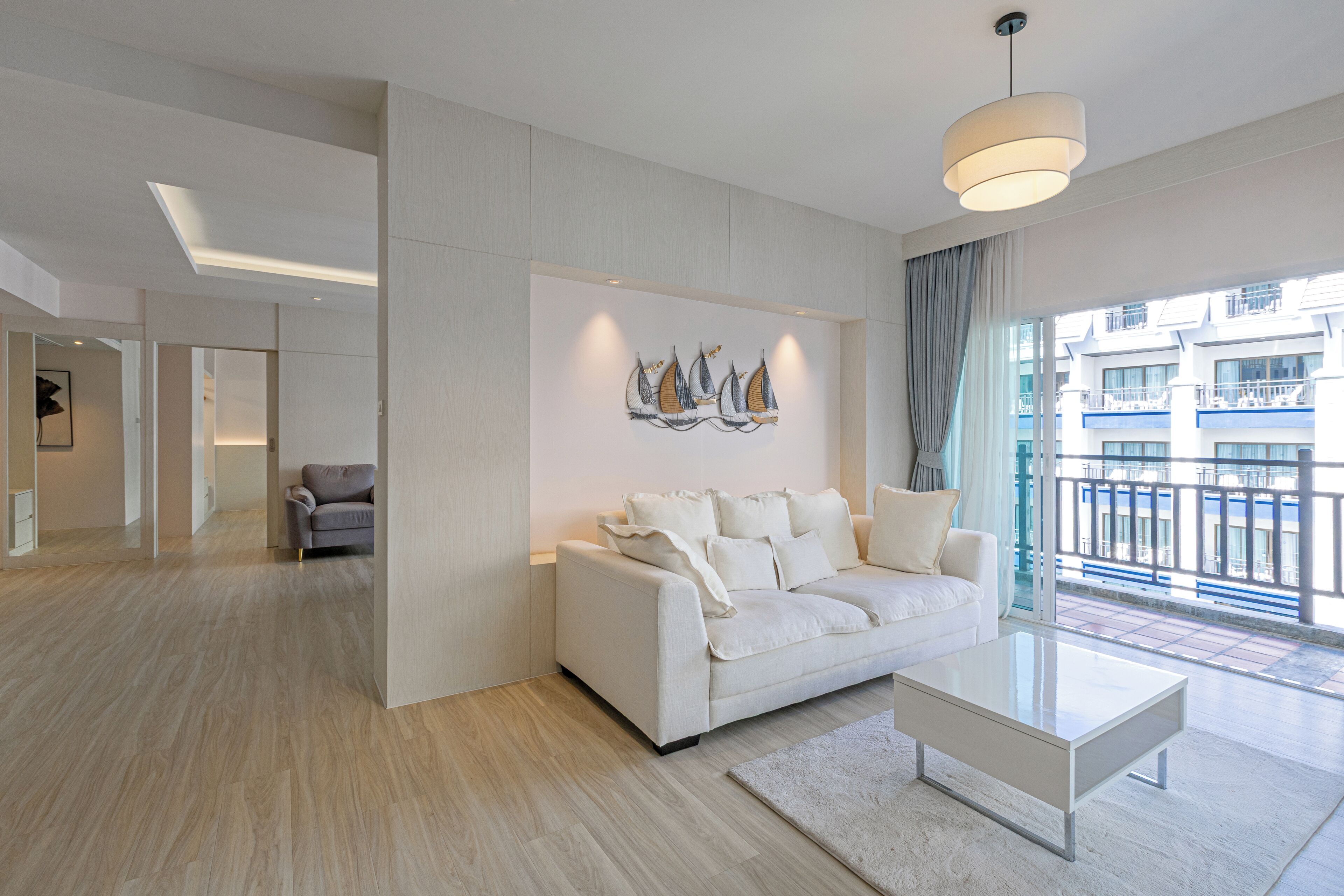 A modern living room with a white sofa, a glass coffee table, and a large window with a view of a building.