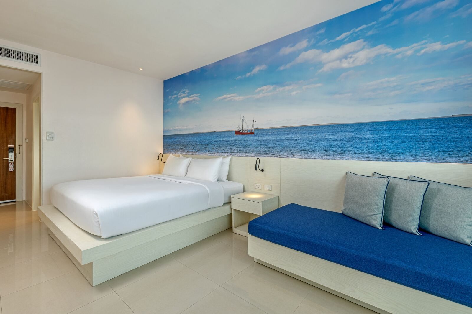Ein Hotelzimmer mit einem Bett, einer Schlafcouch, einem Nachttisch und einem Wandbild mit einer Meereslandschaft.