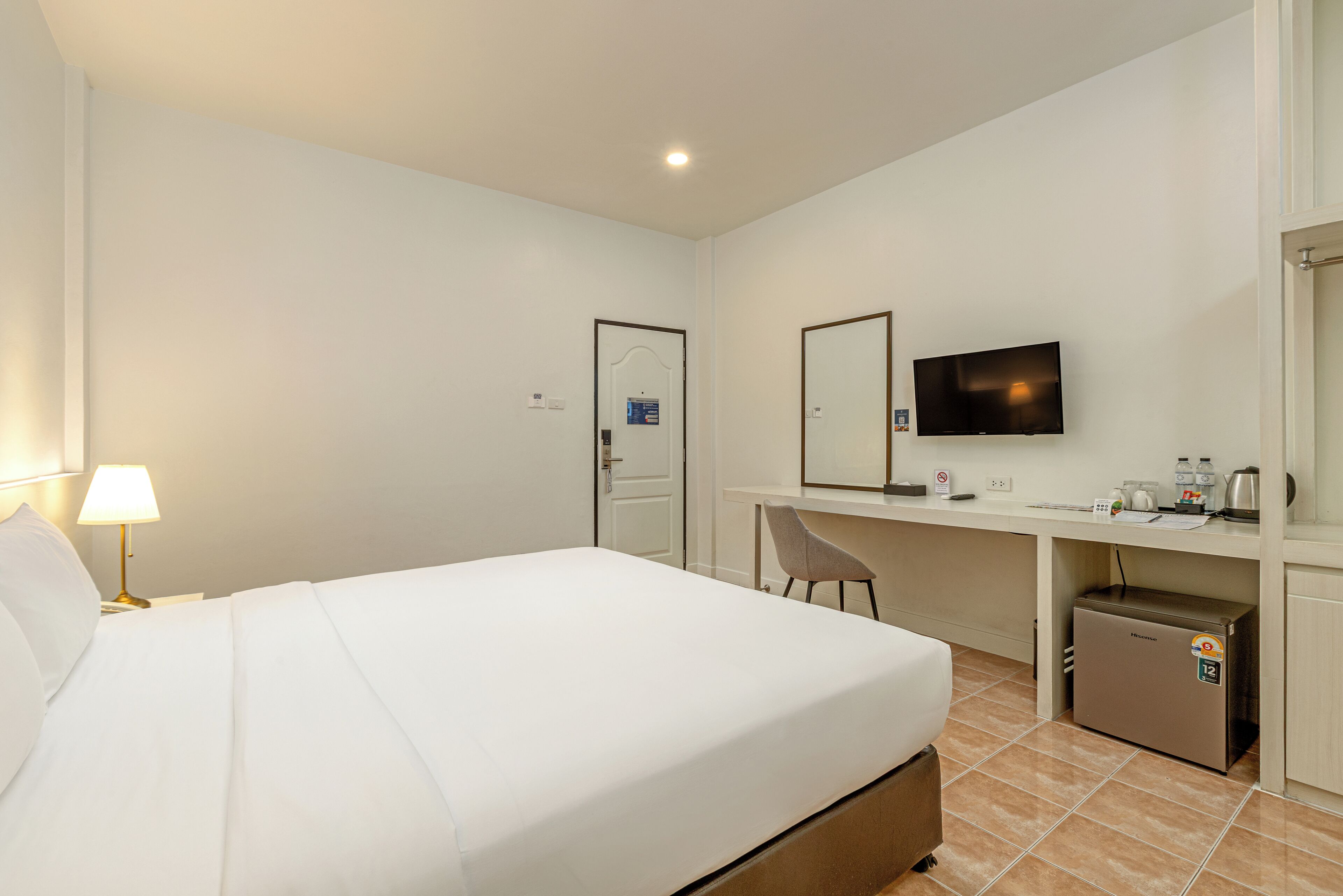A hotel room with a bed, desk, chair, television, and a mini-fridge.