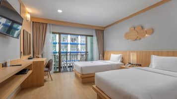 Habitación de hotel con dos camas, un escritorio, una silla, un televisor y un balcón con vistas a edificios.