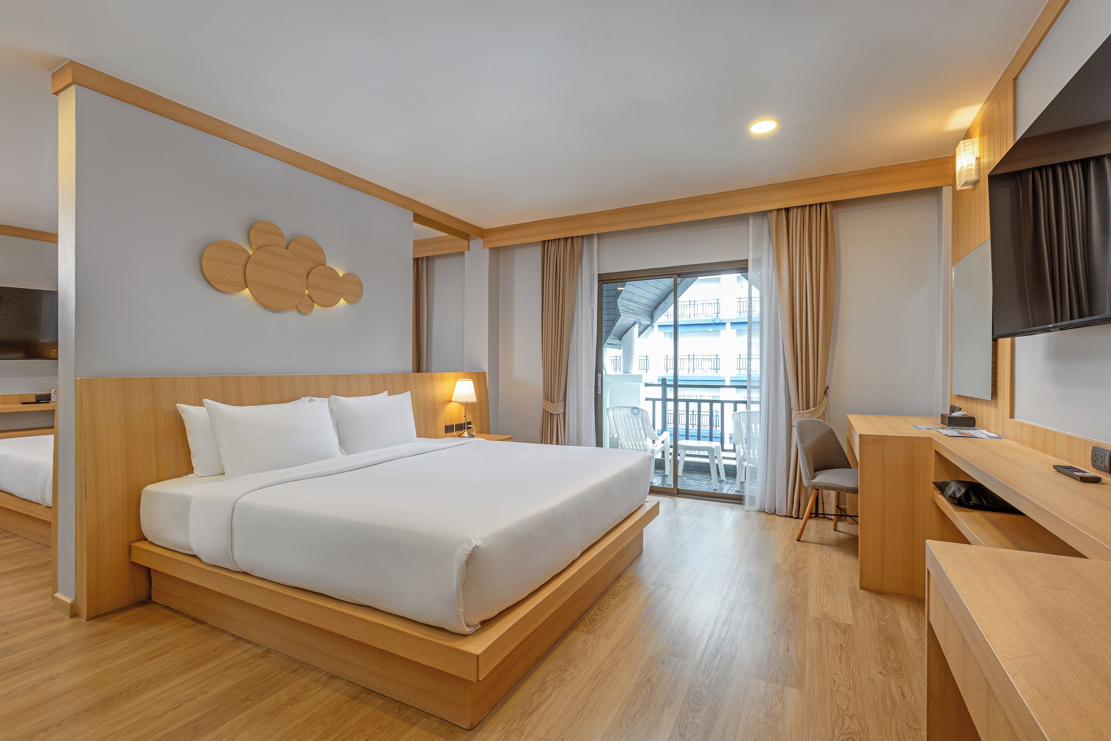 A hotel room with a large bed, a desk, a chair, and a balcony with a view.