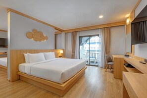 A hotel room with a large bed, a desk, a chair, and a balcony with a view. - Amata Patong (Patong)
