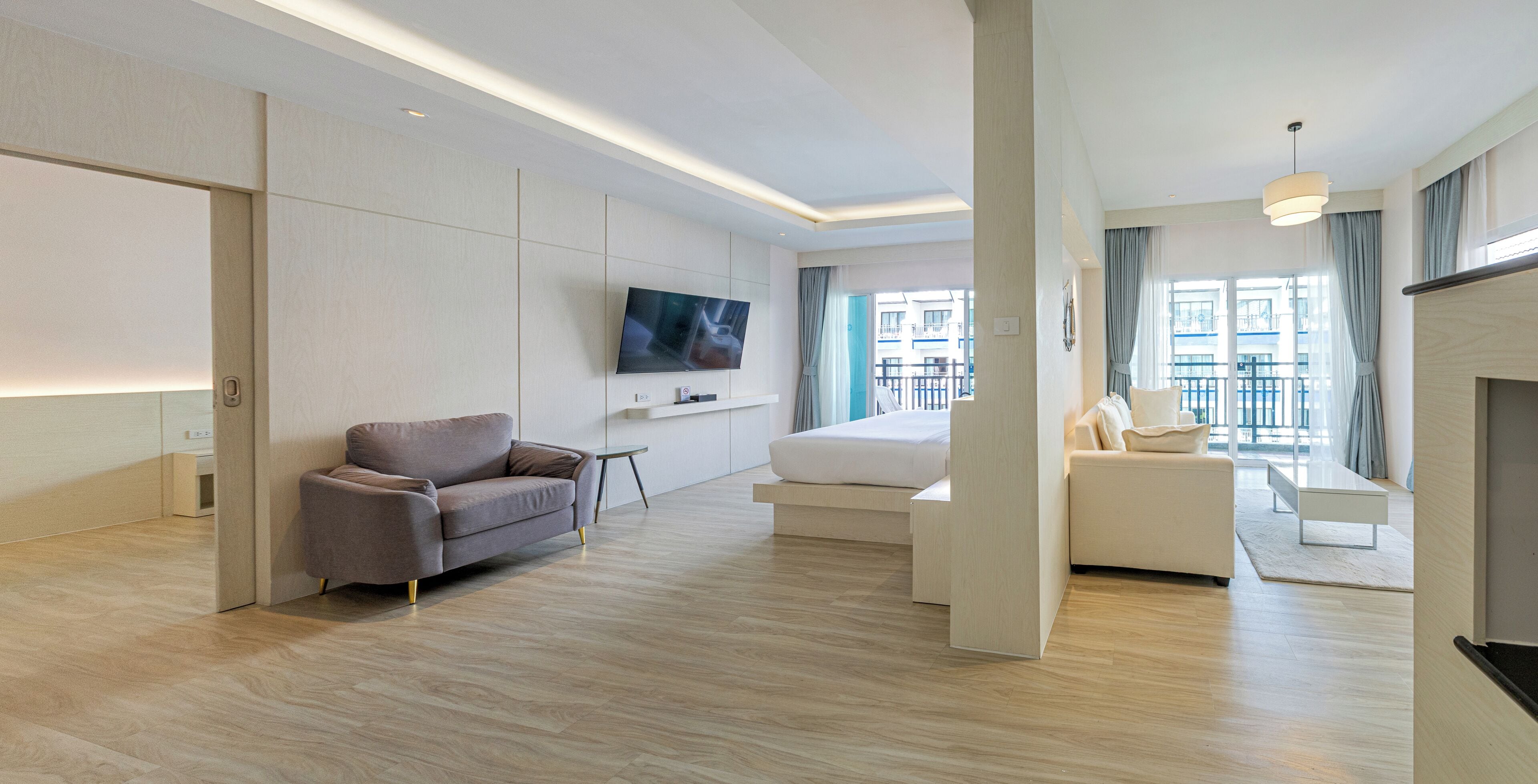 A modern hotel room with a flat-screen TV, a sofa, a bed, and a balcony with a view of the city.