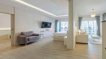 A modern hotel room with a flat-screen TV, a sofa, a bed, and a balcony with a view of the city.