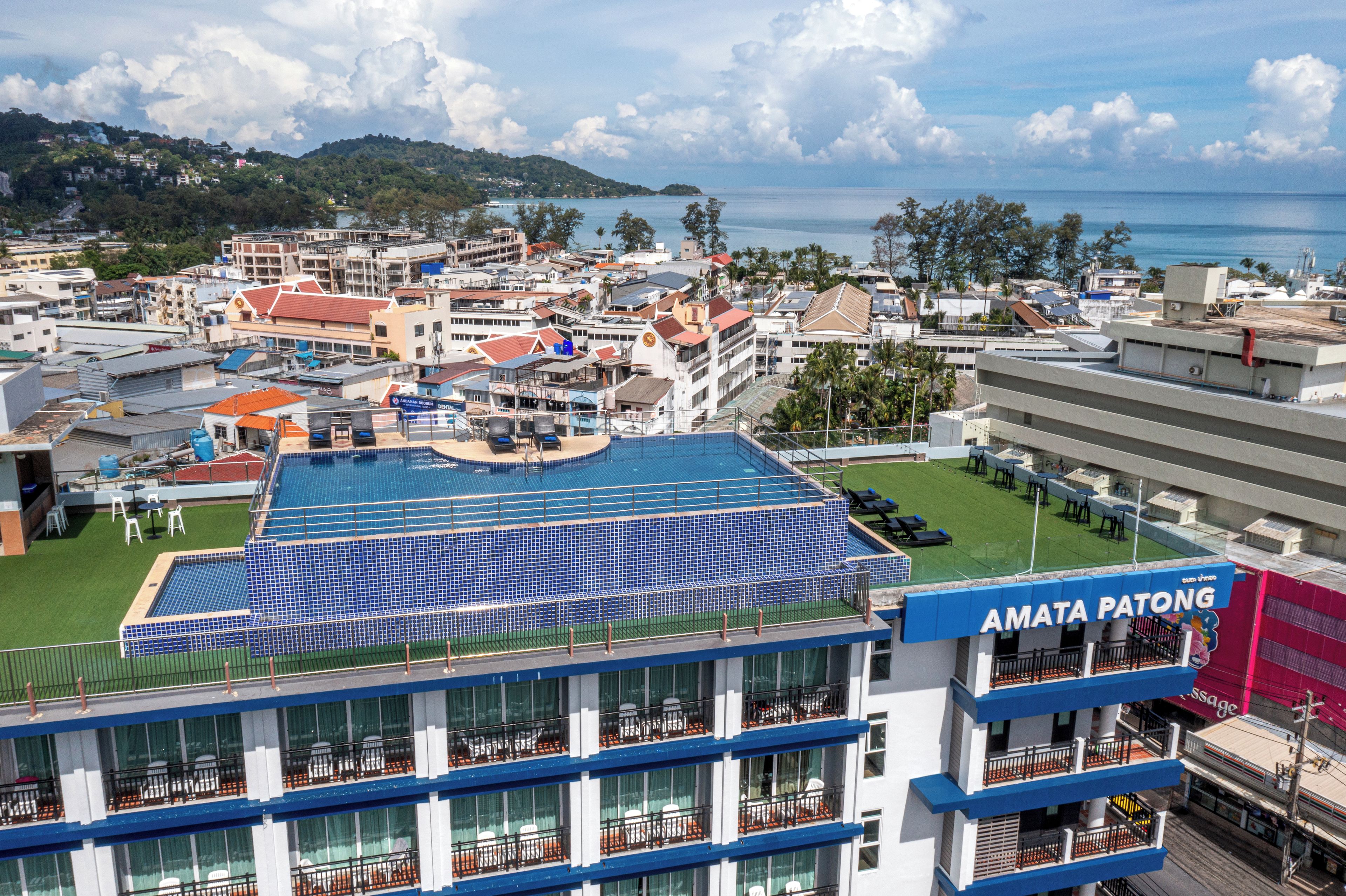 A hotel with a rooftop pool, multiple balconies, and a view of the surrounding town and sea.