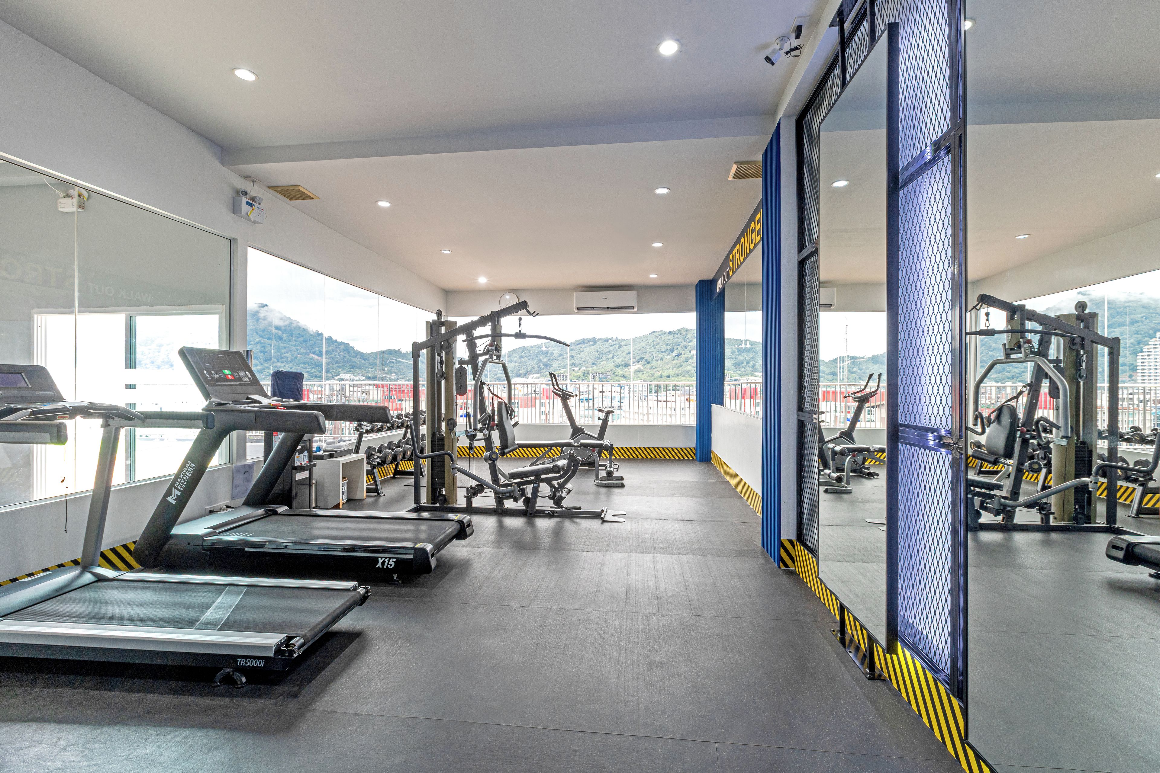Un gimnasio con cintas de correr, máquinas de pesas y un amplio ventanal con vistas a un paisaje montañoso.