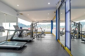 Un gimnasio con cintas de correr, máquinas de pesas y un amplio ventanal con vistas a un paisaje montañoso.
