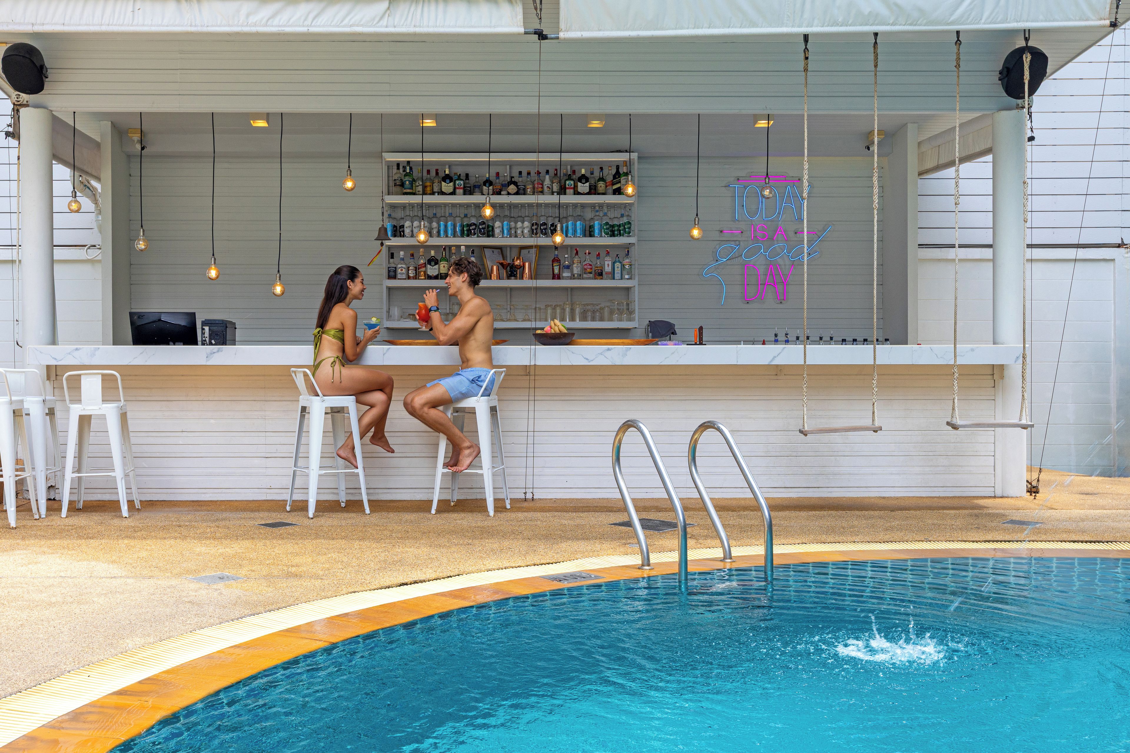 A poolside bar with a bar counter, seating, and a pool with a diving board.