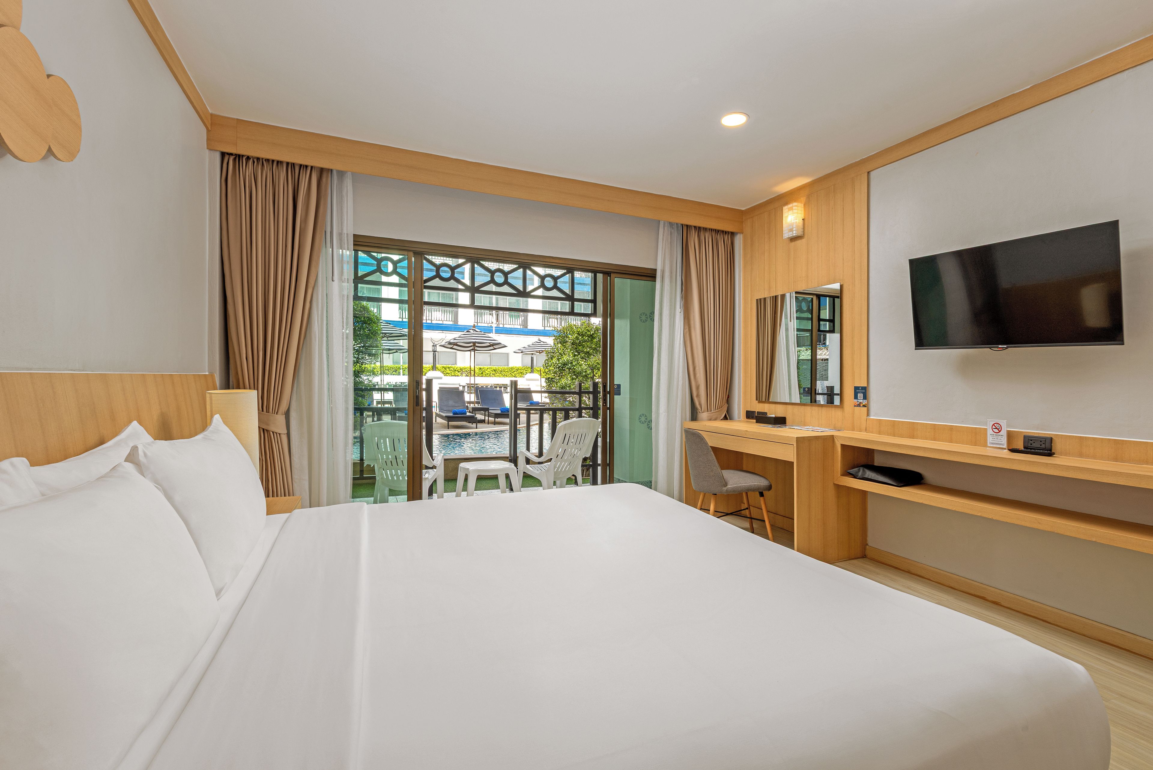 Habitación de hotel con una cama grande, un escritorio, un televisor de pantalla plana y vistas a la piscina exterior.