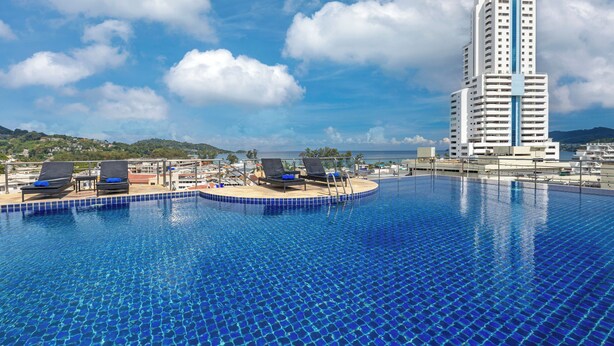A swimming pool with lounge chairs and a view of a tall building in the background. - Amata Patong (Patong)
