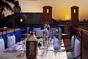 A table set for dining with a sunset view, a decorative lantern, and a blue railing.