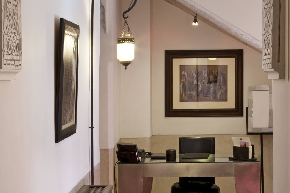 Un couloir intérieur orné d’une arche décorative, un bureau avec un ordinateur, une œuvre d’art encadrée au mur et un luminaire suspendu.