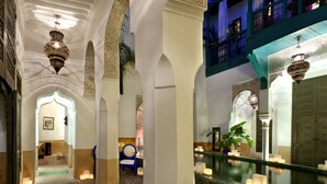 A corridor with ornate arches, a patterned floor, and a pool area with a tiled edge. - Le Farnatchi (Marrakech)