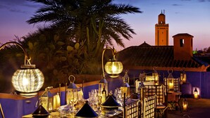 An outdoor dining area with tables set for a meal, surrounded by lanterns and palm trees. - Le Farnatchi (Marrakech)
