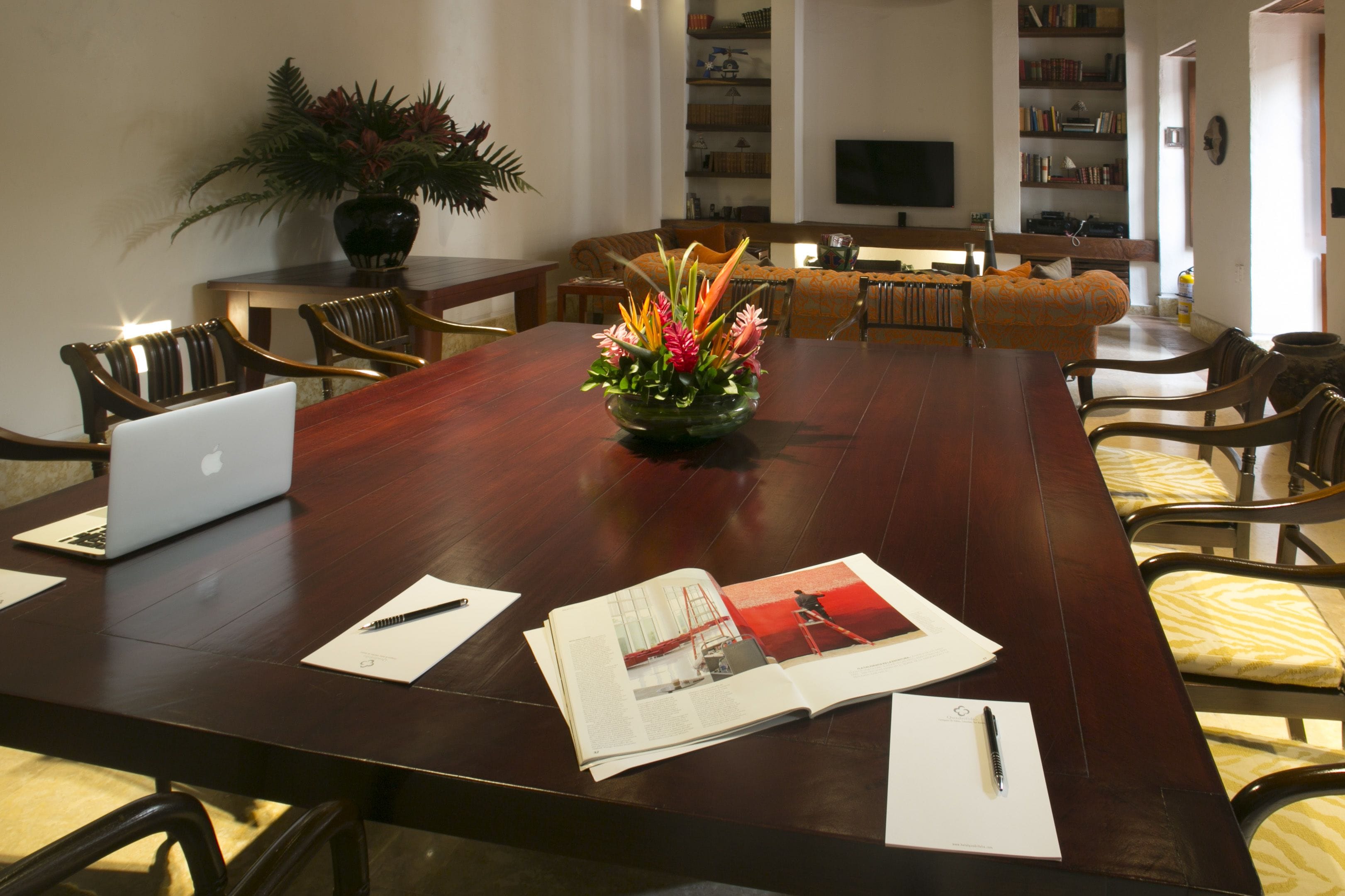 A conference room with a long table, chairs, laptops, documents, and a decorative plant.
