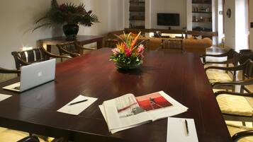 Un salón de conferencias con una larga mesa, sillas, computadoras portátiles, documentos y una planta decorativa.