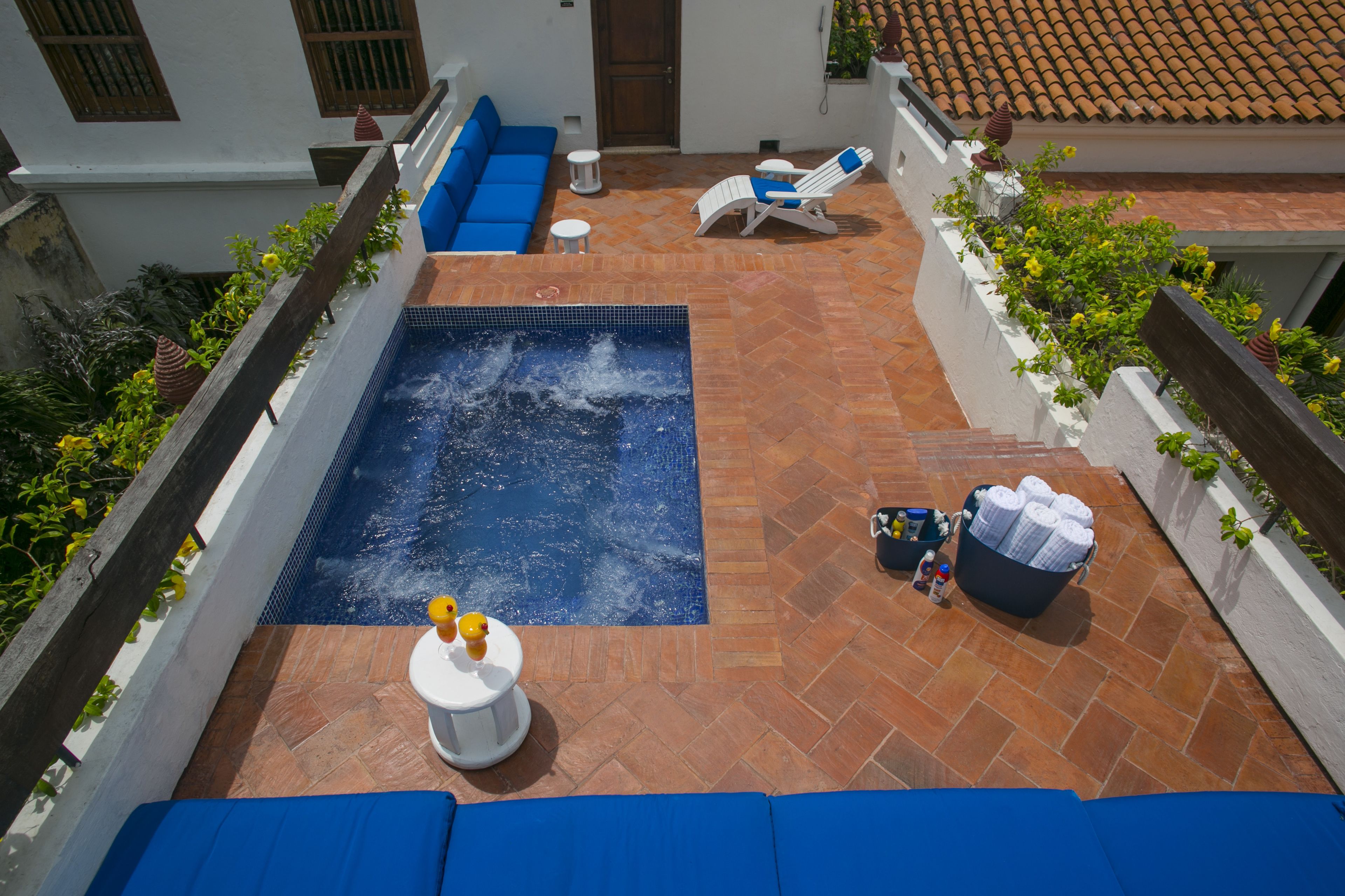 A rooftop pool area with a blue pool, lounge chairs, and a small table with drinks.
