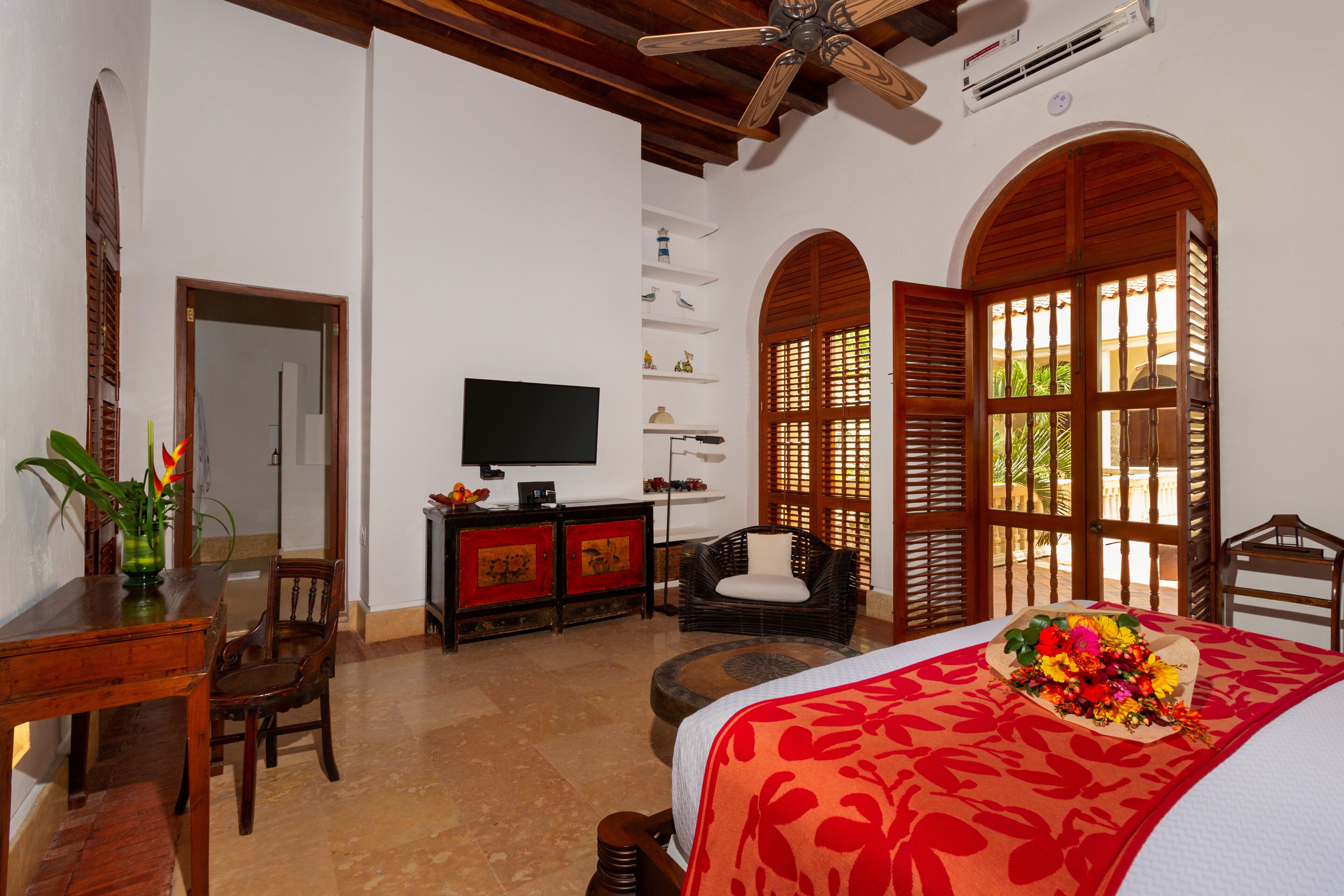 Habitación de hotel con cama, televisor, zona de comedor con mesa y sillas, y estante decorativo en la pared.