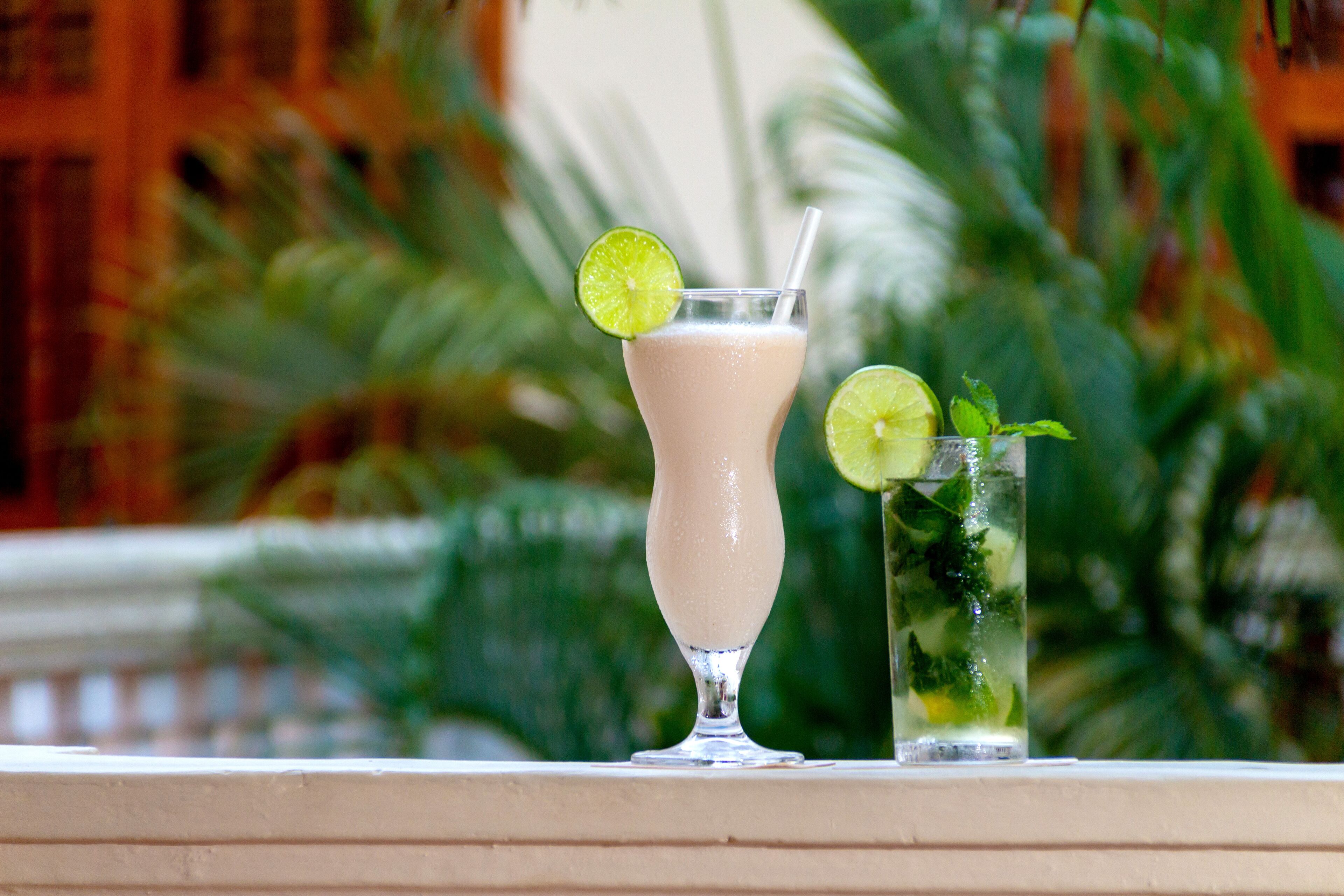 Two drinks on a balcony with a blurred background of greenery and a building.