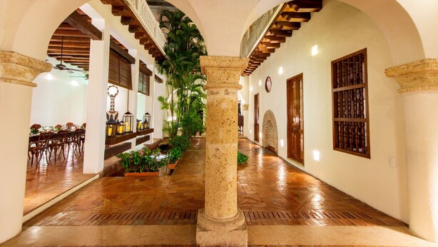 An indoor corridor with arches, a central column, and a dining area with tables and chairs. - Hotel Quadrifolio (Cartagena)