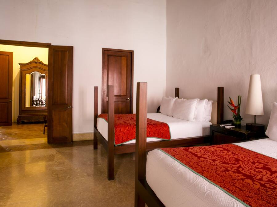 A hotel room with two beds, a wooden wardrobe, a bedside table with a lamp, and a mirror.