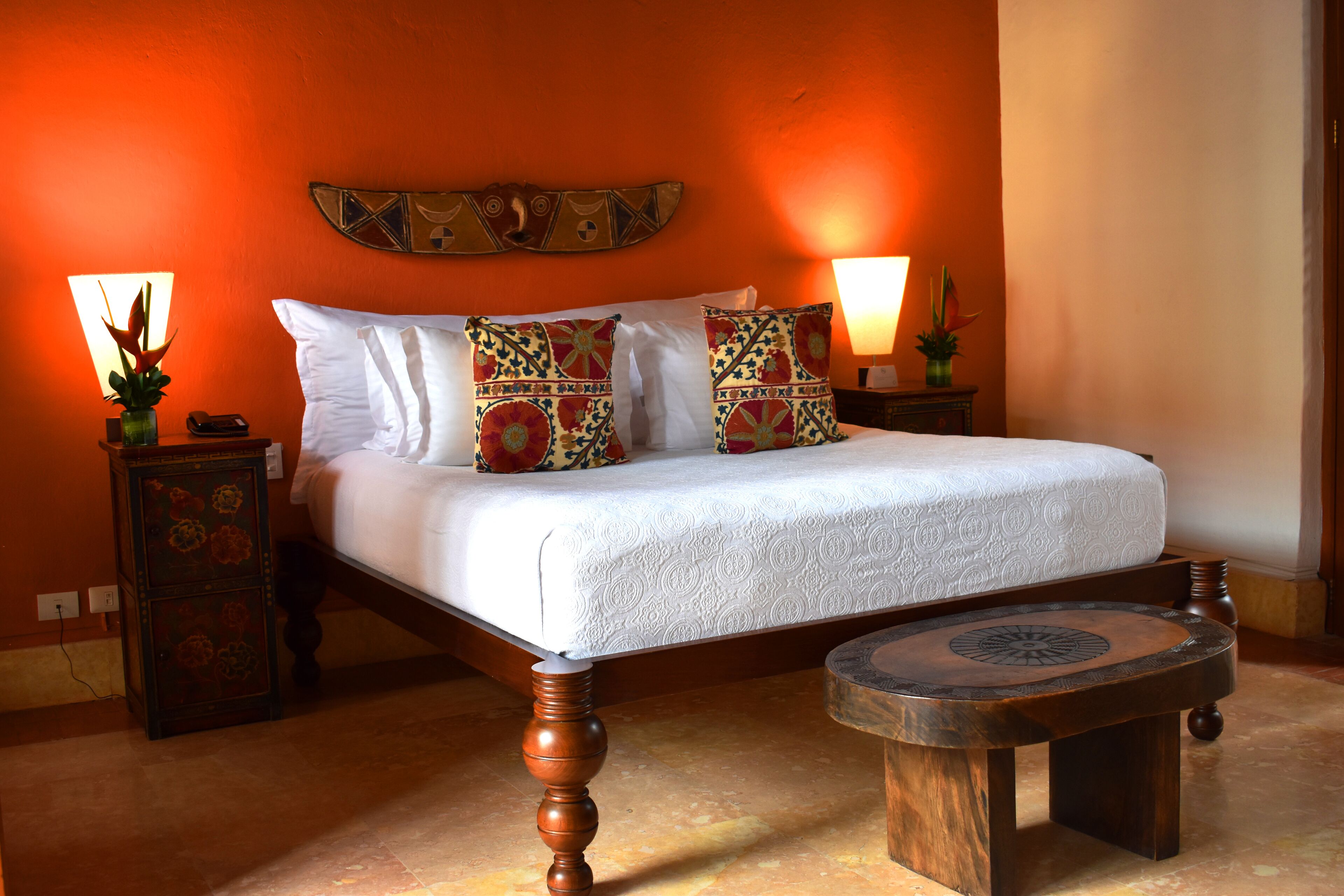 Une chambre à coucher comprenant un lit, deux tables de chevet, une table ronde en bois et un élément décoratif mural.