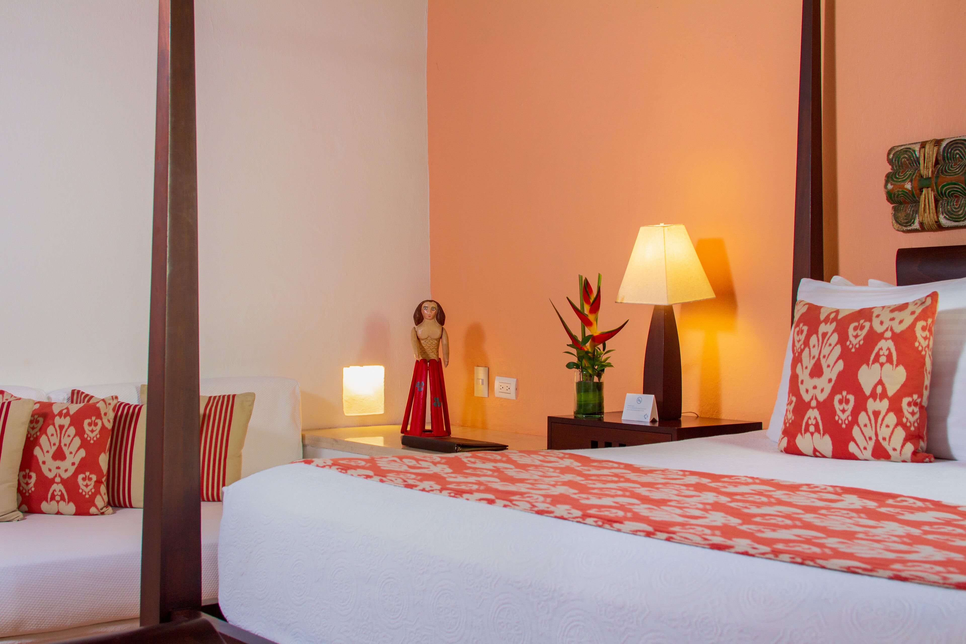 Habitación de hotel con cama, mesita de noche, lámpara, estatua y un florero con flores.