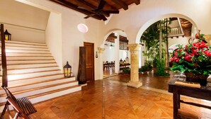 A spacious hallway with a wooden staircase, a ceiling fan, and a potted plant with red flowers. - Hotel Quadrifolio (Cartagena)