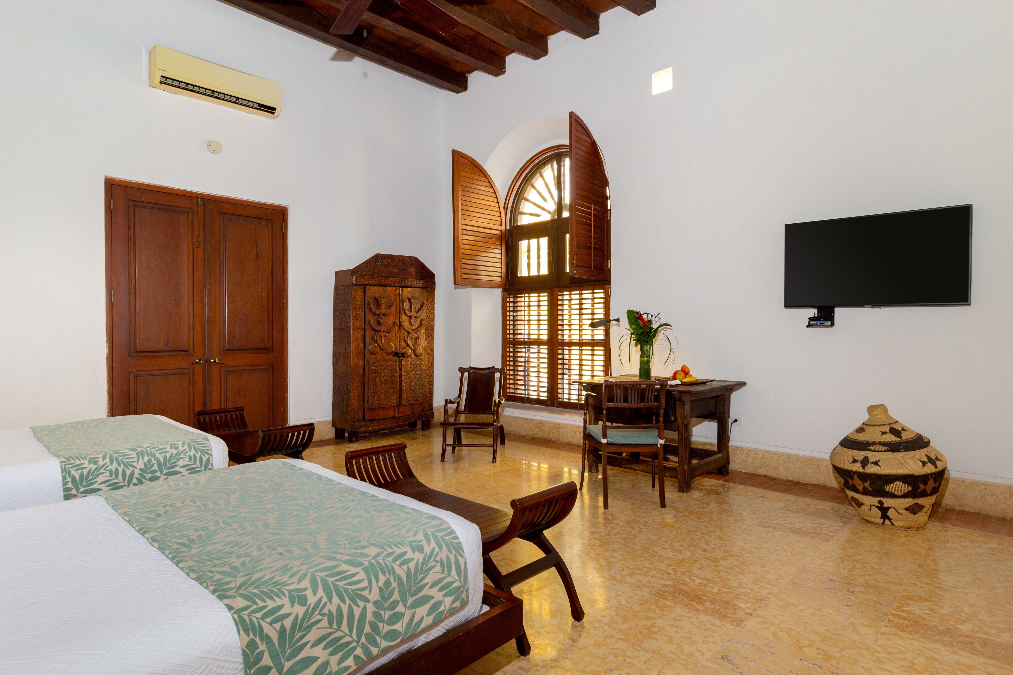 Habitación de hotel con dos camas, un armario de madera, un escritorio con silla, un televisor y un jarrón decorativo.