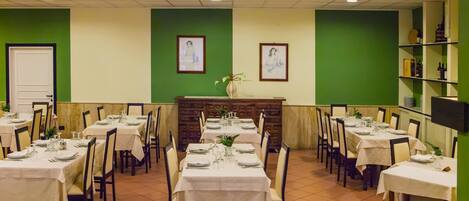 A restaurant with multiple tables set for dining, a reception area, and green walls.