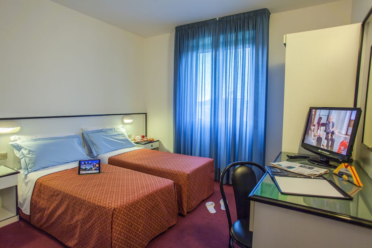 A hotel room with two beds, a desk with a computer, and a TV.