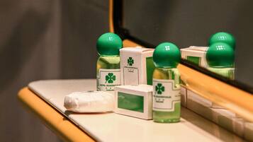 Una encimera de baño con artículos de aseo, incluyendo una botella verde, una blanca y una caja con un logotipo verde.