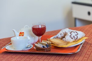 Una bandeja con una tetera, una taza, un vaso de bebida roja y pasteles sobre un mantel a cuadros.