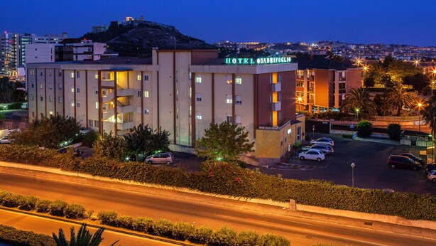 Un hotel con varios pisos, un estacionamiento y vista panorámica del paisaje urbano al fondo.