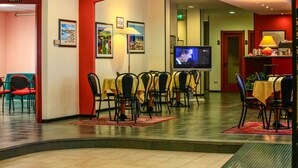 Un comedor de hotel con mesas y sillas, un televisor y obras de arte en las paredes.