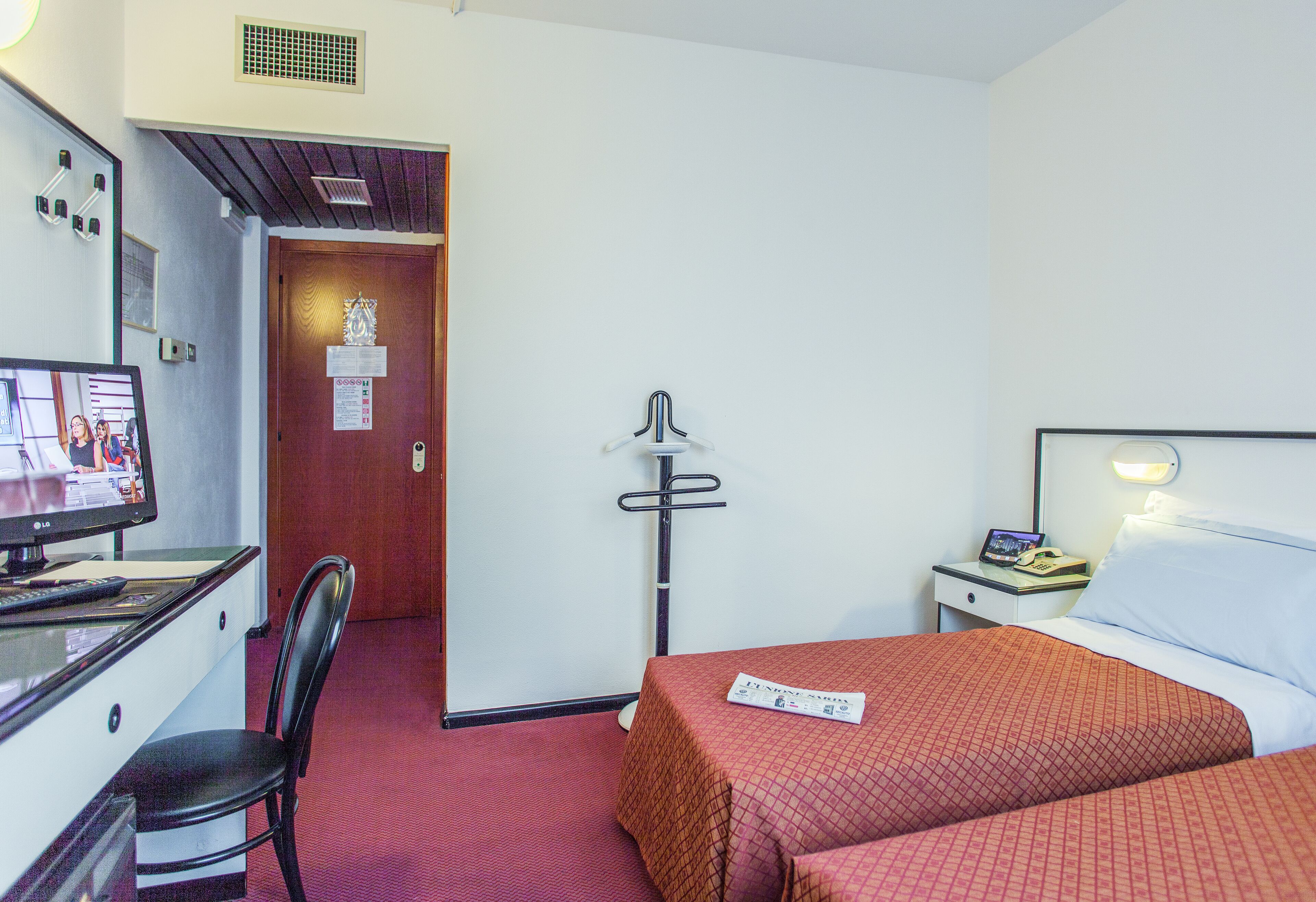 Quarto de hotel com escrivaninha, cadeira, cama e abajur.