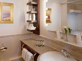 Un baño moderno con encimera de granito, un lavabo blanco y un espejo encima. Hay estantes con artículos de aseo y un perchero con toallas.
