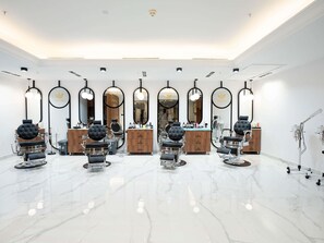 Un salón de belleza con varias estaciones de peluquería, cada una con espejo y sillón, y un tocador de madera.