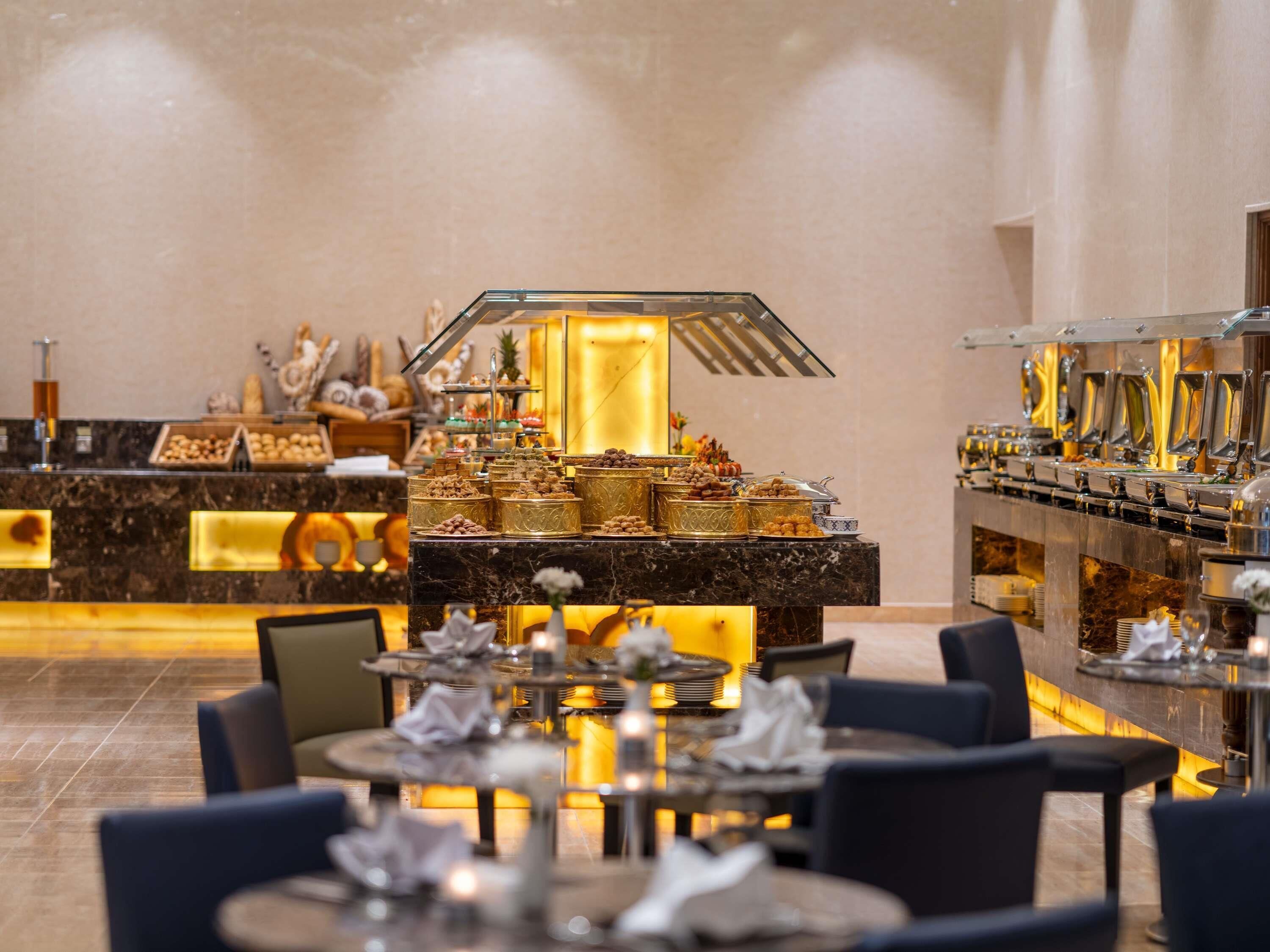 Un vestíbulo de hotel con una recepción de mármol, una zona de buffet con diversas opciones de comida y arreglos de asientos.