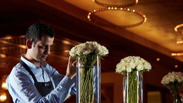 A person arranging white flowers in a glass vase on a table with white stones.