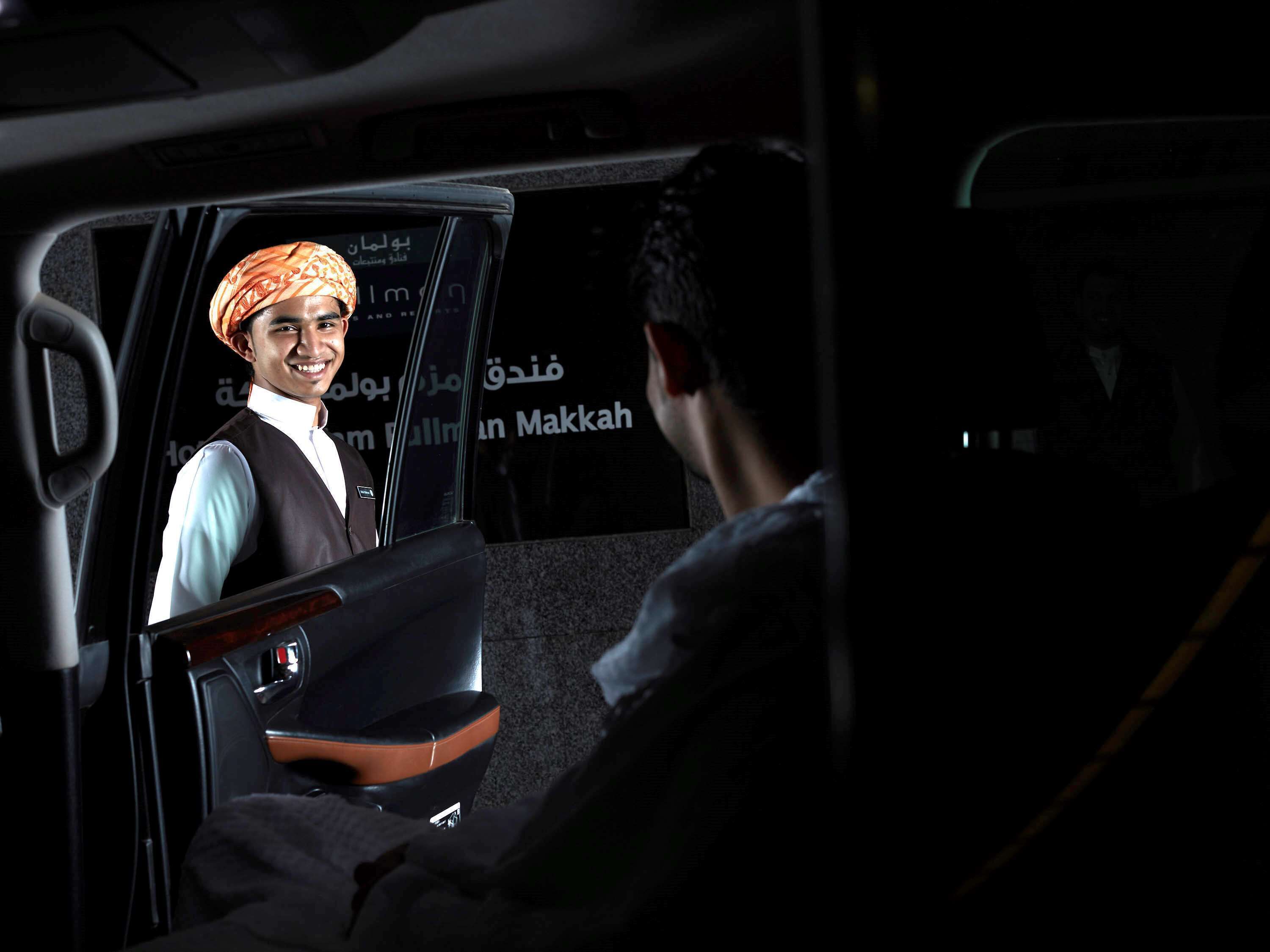 A car interior with a person seated in the back seat and another person standing in the driver's seat.