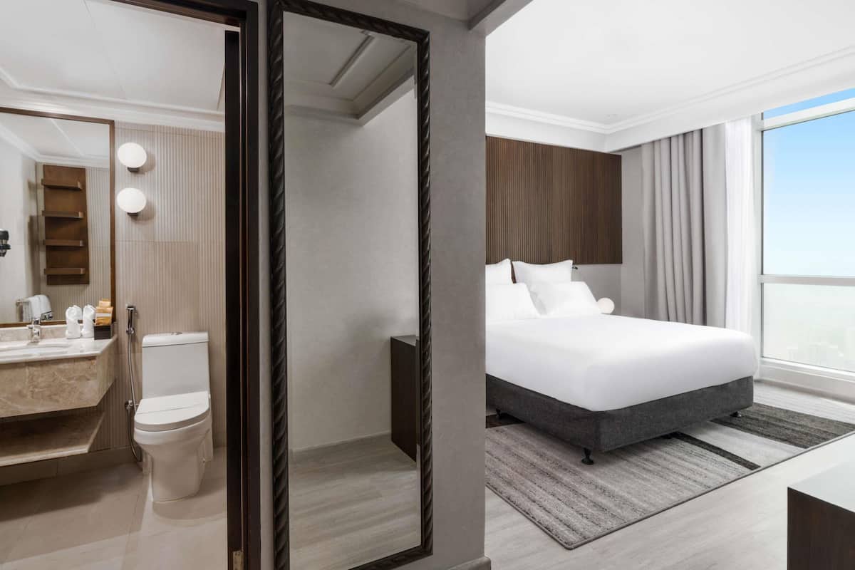 A modern hotel room with a large bed, a bathroom with a vanity, and a view of the sky.