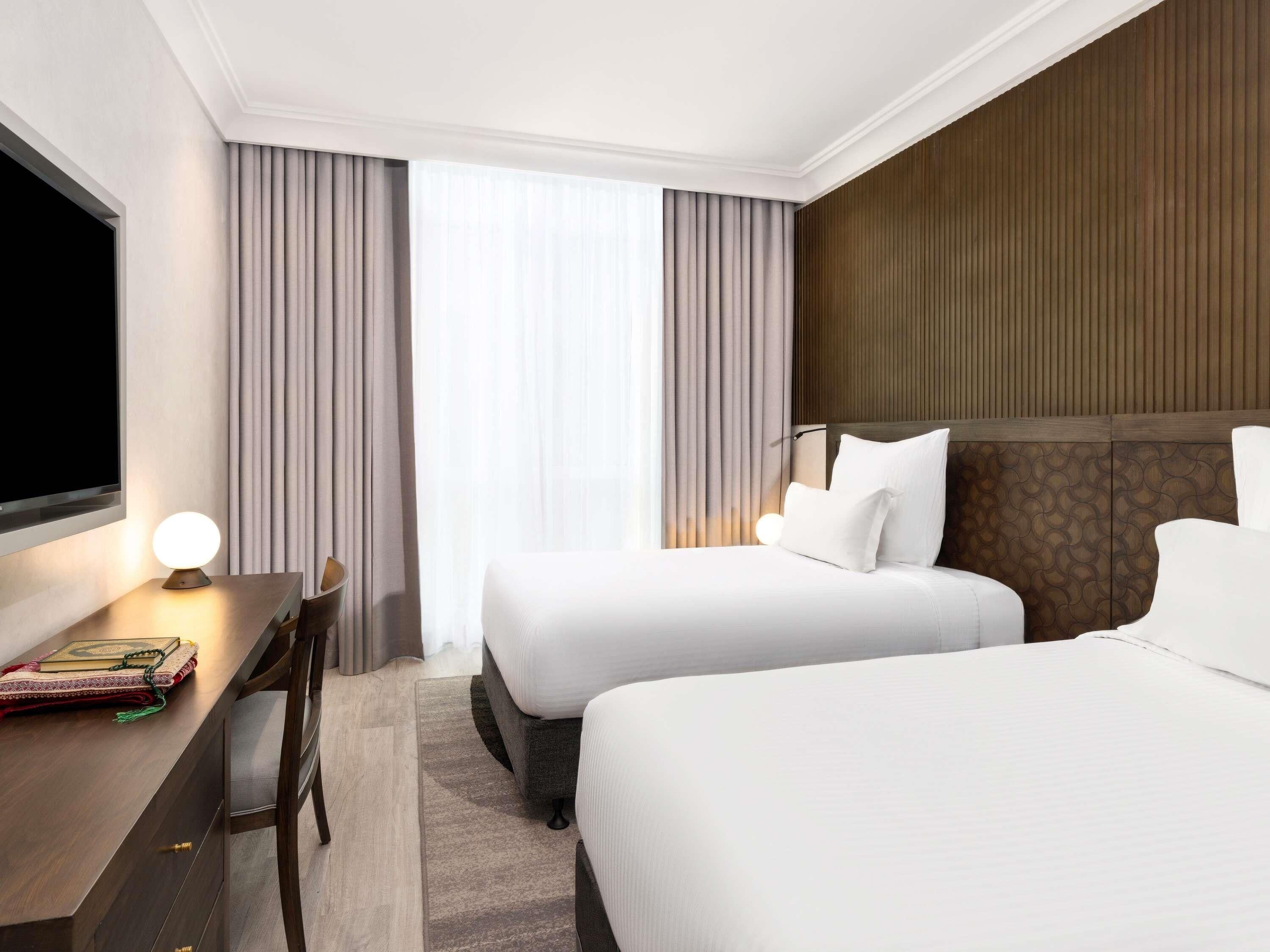 Une chambre d’hôtel avec deux lits, un bureau avec une lampe, une télévision et une fenêtre avec des rideaux.
