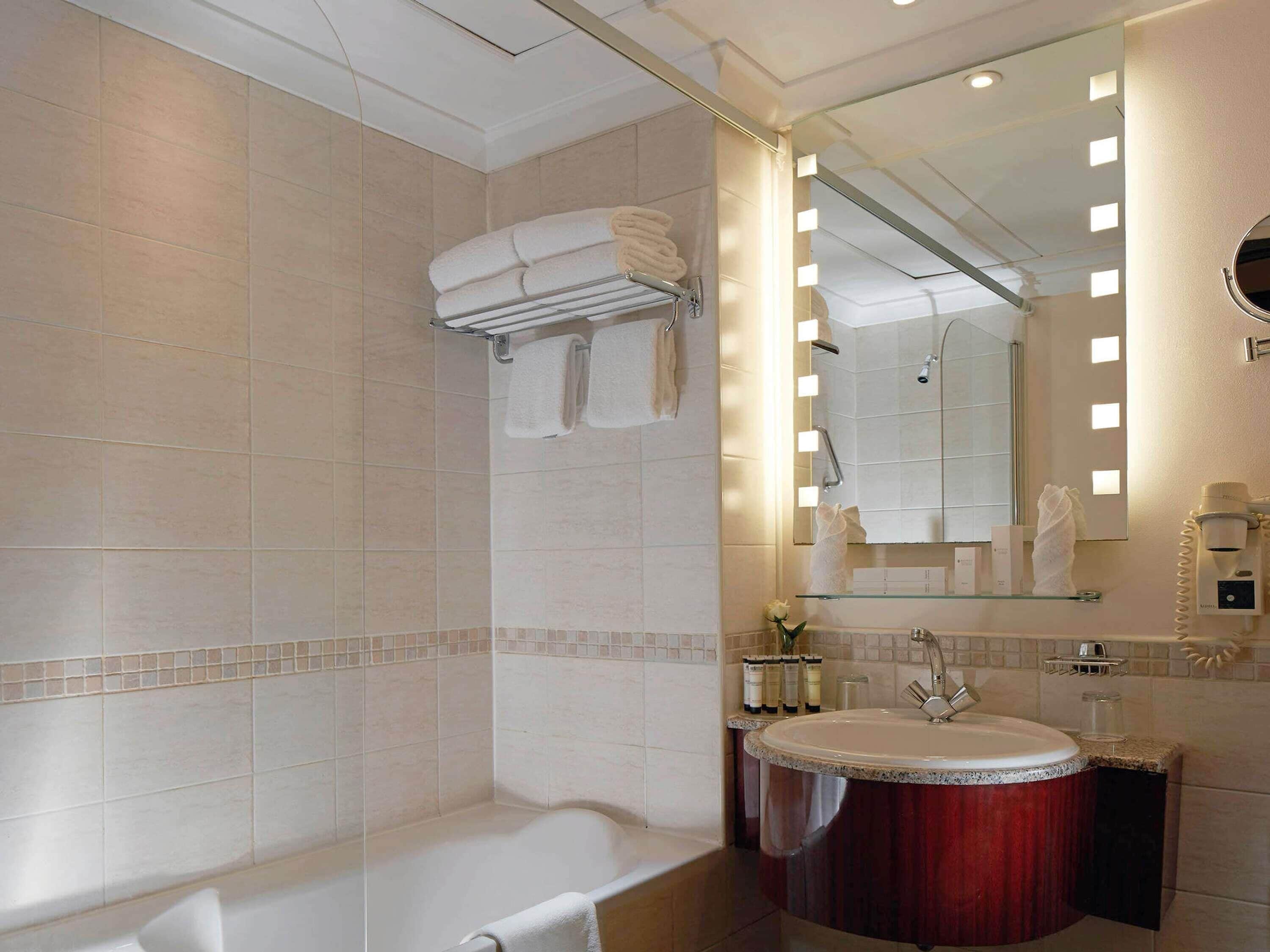 Un baño moderno con bañera, tocador con lavabo y un espejo grande con iluminación.