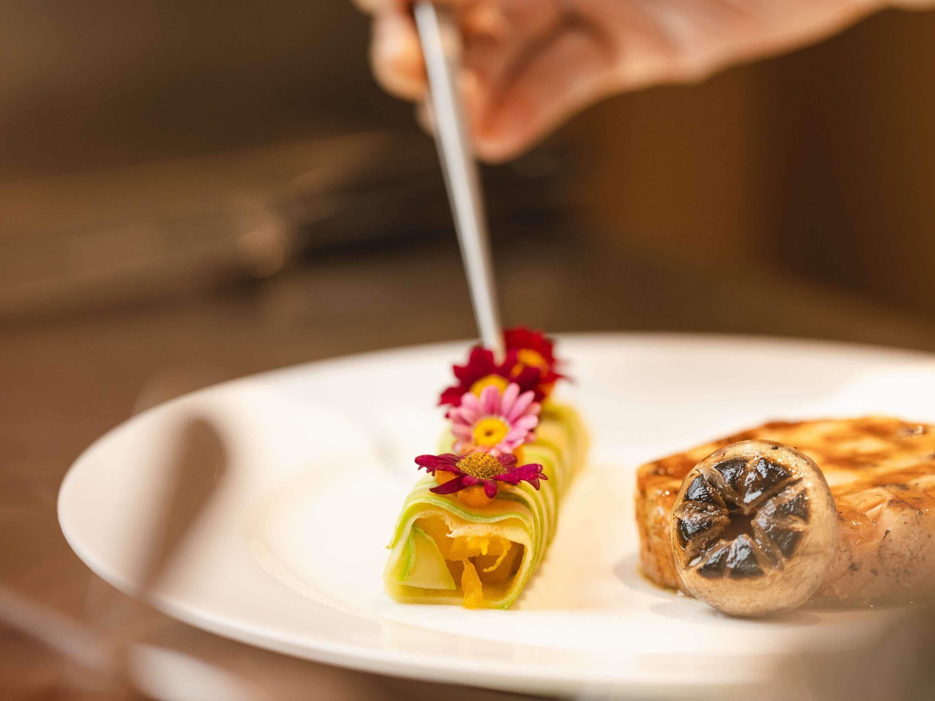A hand cutting a rolled pastry with a flower garnish on a white plate.
