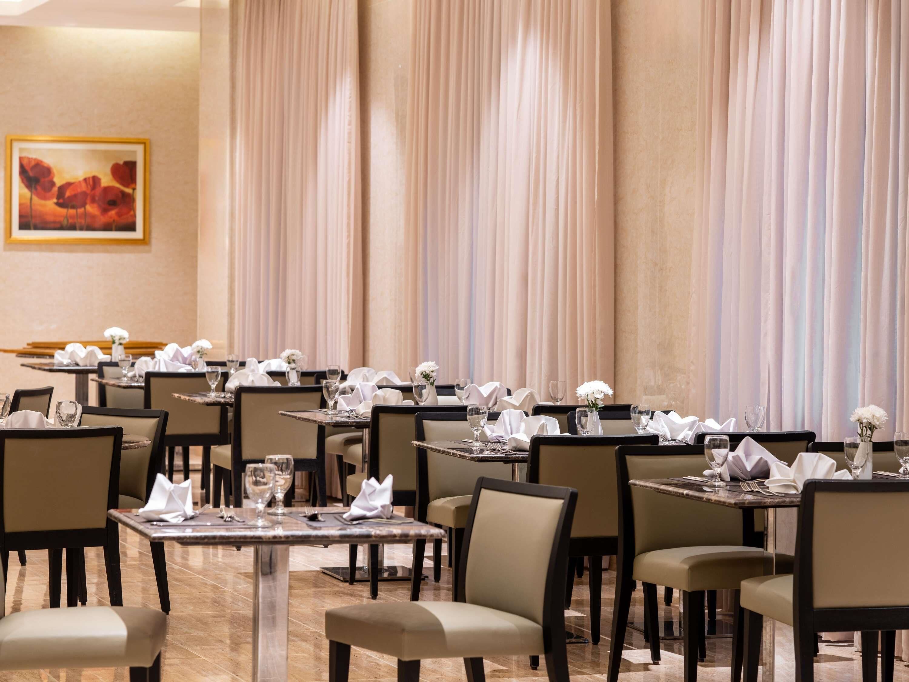 A restaurant with multiple tables, chairs, and a painting on the wall.