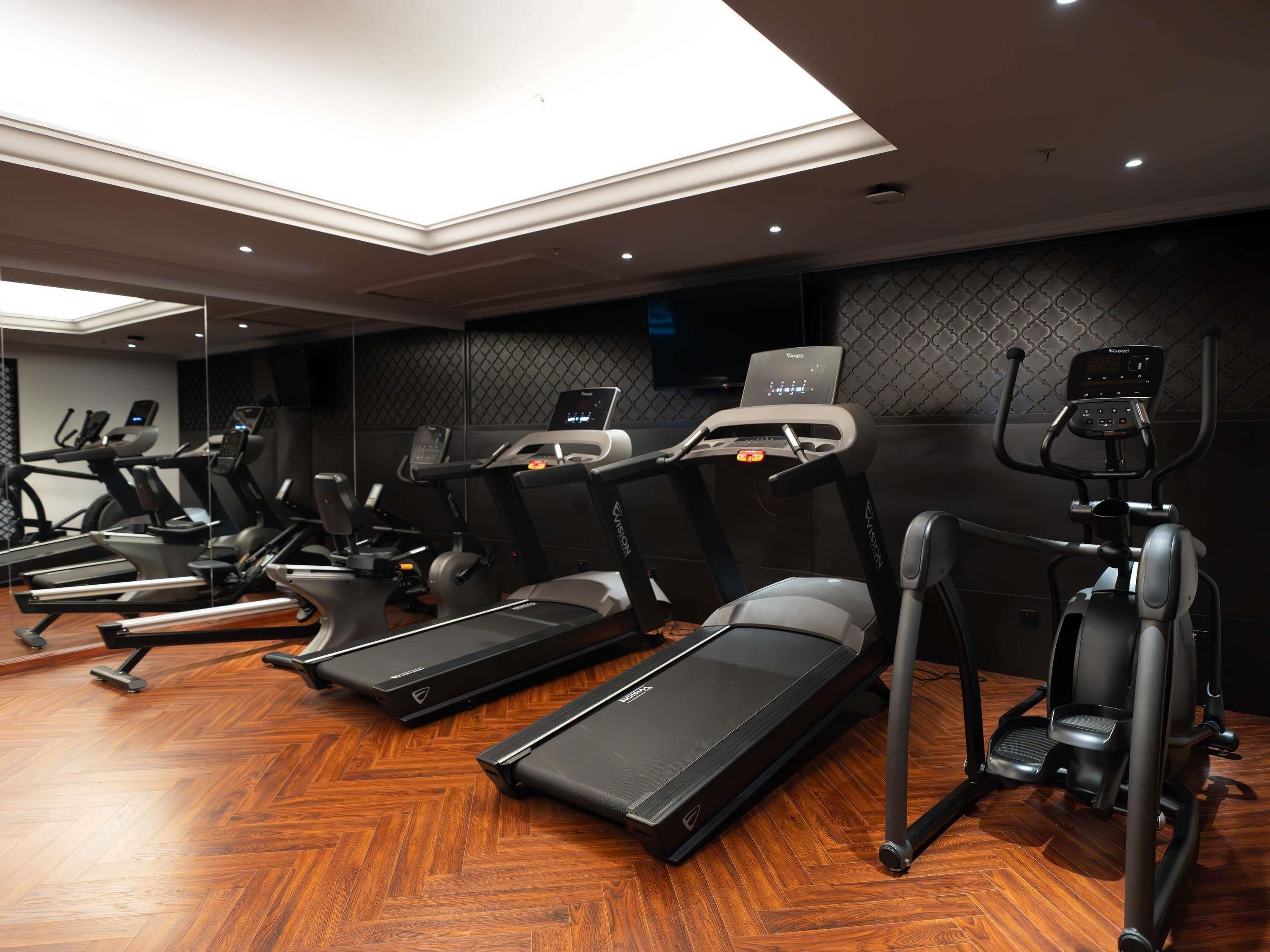 A gym with treadmills, elliptical machines, and a mirrored wall.